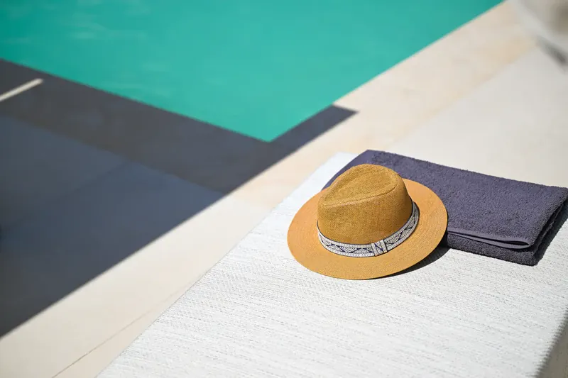 A straw hat and towel at the edge of the pool